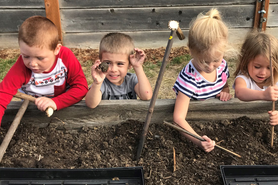Four kids play in the first with sticks in a garden bed