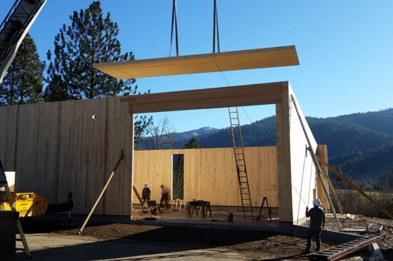 A wooden board is lowed down onto the frame of a home in construction