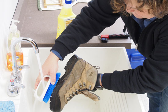 A person brushes the sole of a hiking boot with a brush over a sink