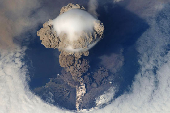 An aerial view of a plume of smoke erupting from a volcano