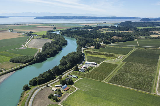 A river winds through farm and fields leading to the ocean in the background