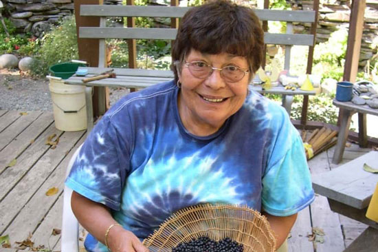 A person in a tie dye tshirt smiles holding a basket of huckleberries